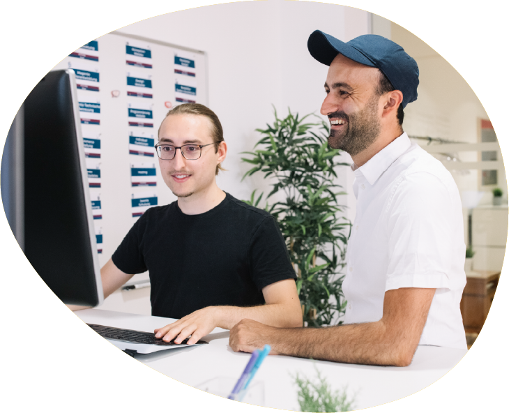 Bild3ady2025 Zwei Männer an einem Schreibtisch mit Computern, lachend – Teamarbeit in einer modernen Büroumgebung.